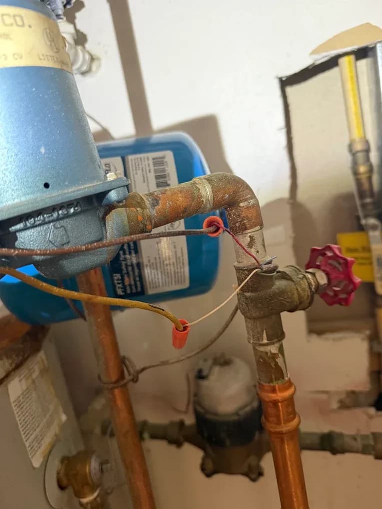 A boiler circulator pump and expansion tank on copper piping during a heating system repair