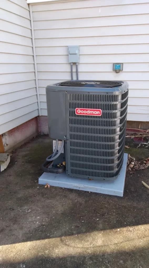 A newly installed outdoor air conditioning condenser sitting on a levelled pad against the siding of a home